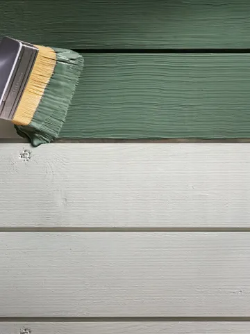 En pensel målar med grön färg på en träfasad