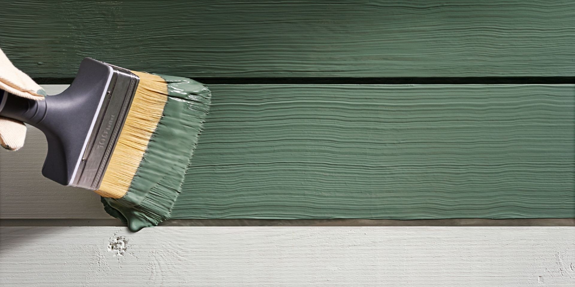 En pensel målar med grön färg på en träfasad