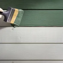 En pensel målar med grön färg på en träfasad